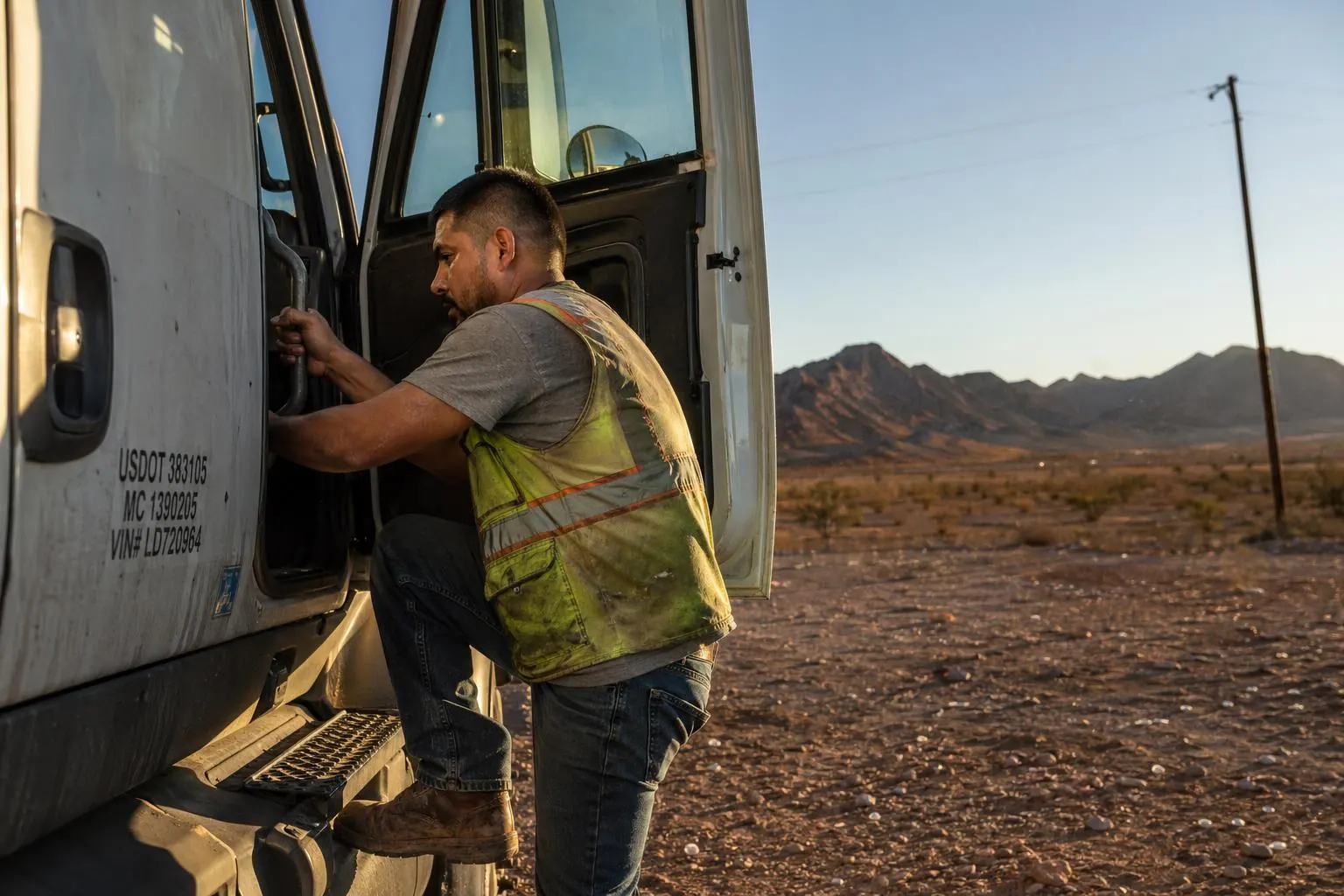 CDL student climbing into the cab of a working semi truck in the El Paso desert at golden hour, Franklin Mountains in the distance